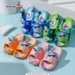 A pair of bright blue and light blue kids' slides with a cheerful 3D shark design on the straps, and small shark cartoon patterns on the footbeds. The slippers have thick, comfortable-looking soles.