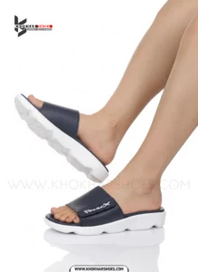 A man's feet in a pair of comfortable, navy blue and white, single-strap slides on a white background.