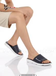 A man's feet in a pair of comfortable, navy blue and white, single-strap slides on a white background.