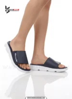 A man's feet in a pair of comfortable, navy blue and white, single-strap slides on a white background.